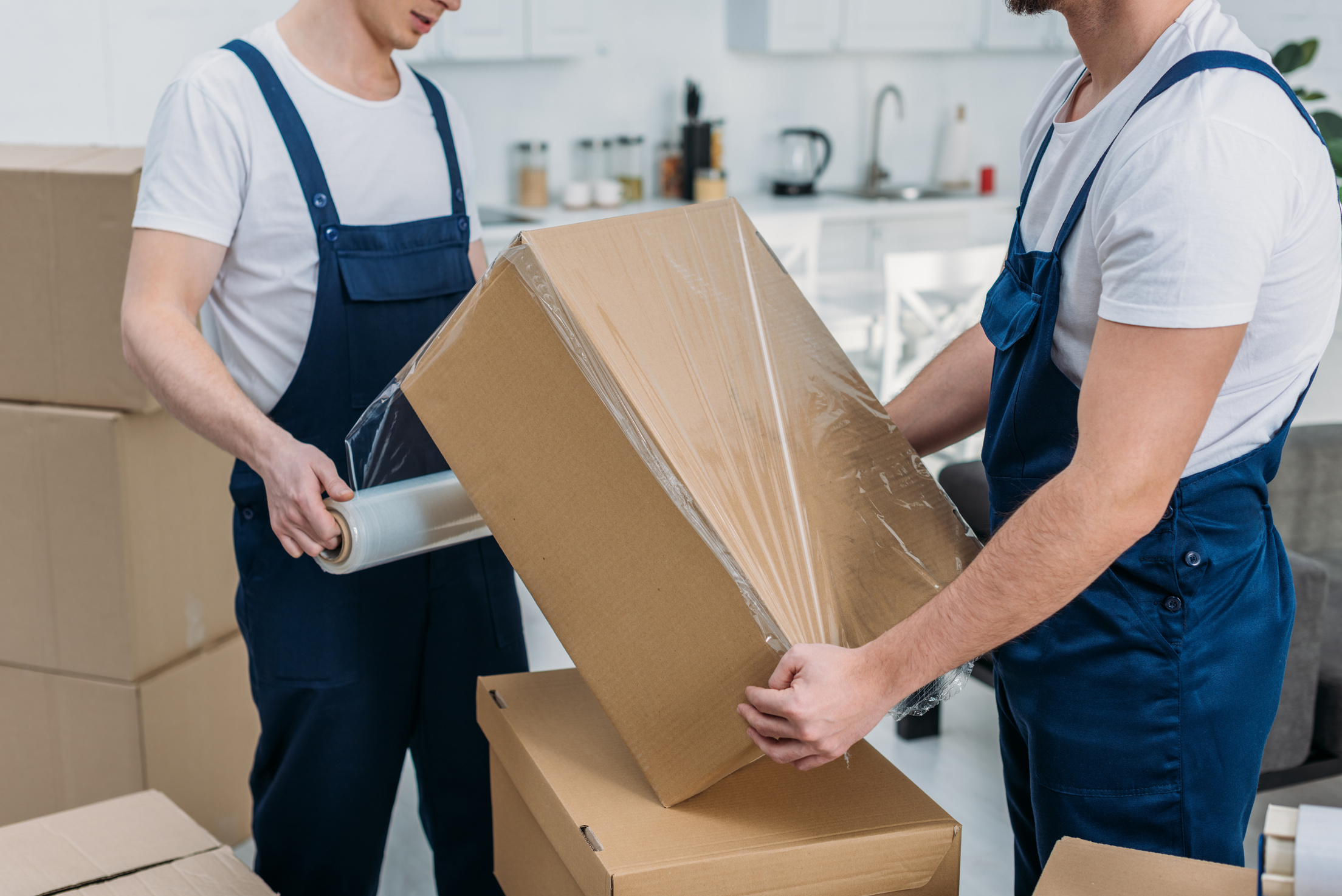 partial view of movers wrapping cardboard box with stretch film in apartment